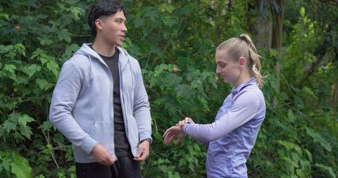 Couple talking on forest trail while woman checking fitness tracker and preparing workout