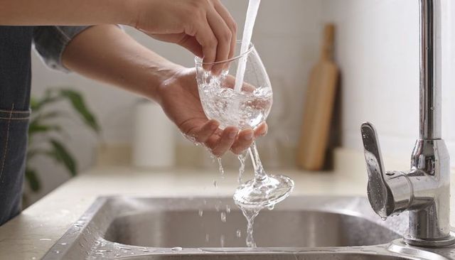 Rinsing wine glass under running tap in modern kitchen sink hands cleaning stemware