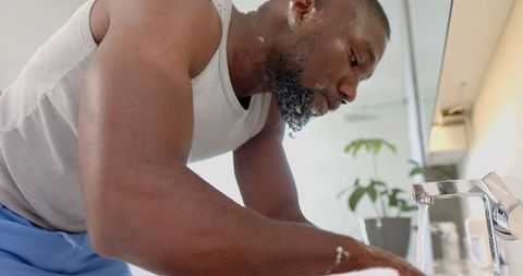 Man washing beard under running faucet for self-care routine