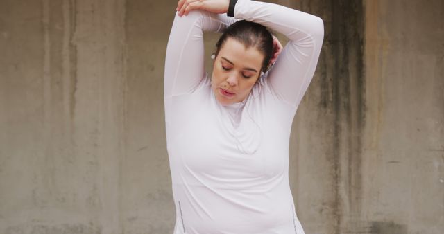 Plus size caucasian woman wearing earphones fitness training in city stretching arms. City living, fitness and modern urban lifestyle.