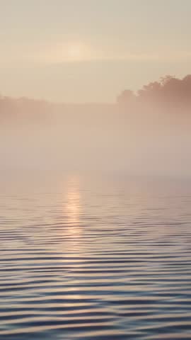 Misty dawn lake with sun column reflection on gentle ripples vertical 9:16 video