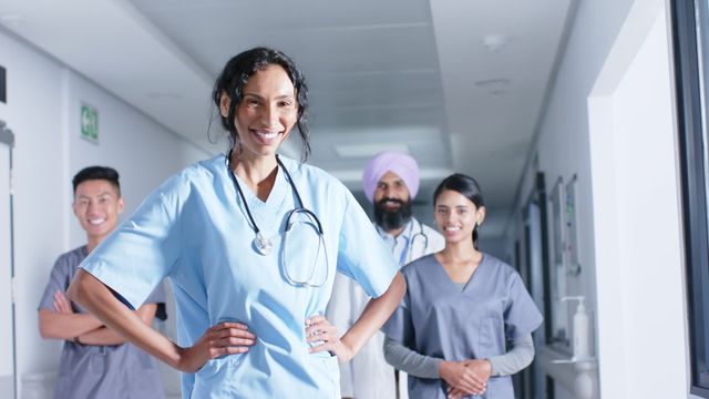 Group of diverse healthcare professionals confidently smiling in hospital corridor, showcasing unity and professionalism in healthcare settings. Useful for illustrating teamwork, diversity, and inclusivity in medical environments. Suitable for articles, training material, and promotional campaigns related to healthcare services.