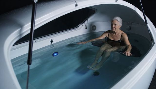 Senior woman floating in private hydrotherapy pod with calming blue led light