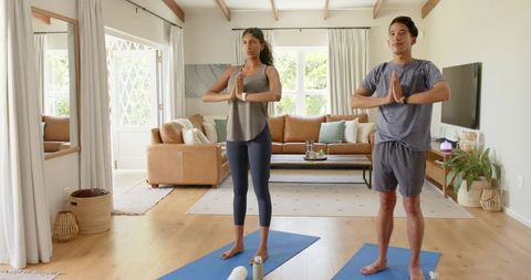 African american couple practicing yoga at home on blue mats in sunlit living room