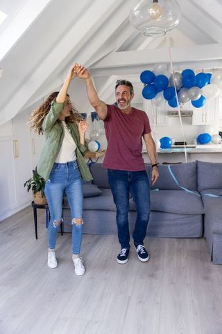 Middle-aged couple dancing in modern loft living area with blue balloons and streamers