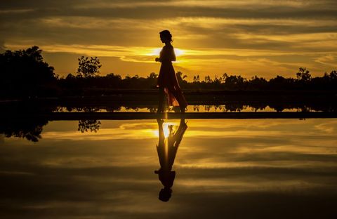 Silhouette of Woman Walking Along Tranquil Lakeside at Sunset