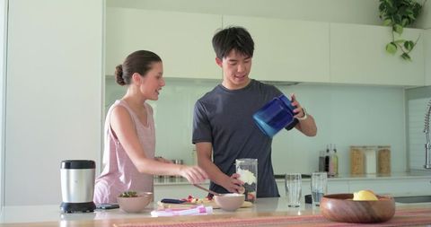 Couple making smoothies together in modern kitchen pouring yogurt and fresh fruit