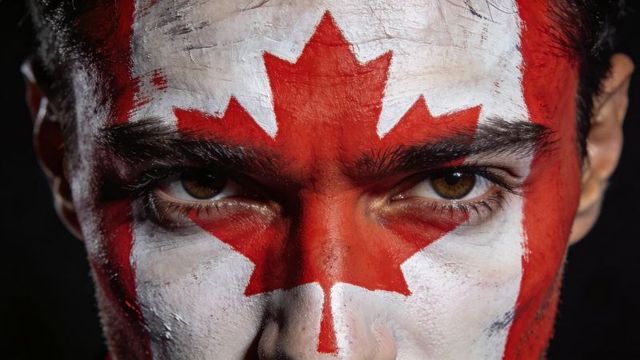 Intense closeup male wearing canadian flag face paint with bold maple leaf