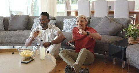 Diverse friends gaming on living room floor with snacks and bottled drinks