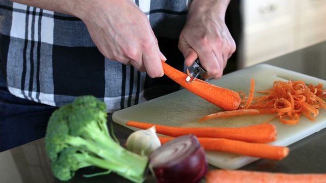 Hands shown peeling fresh carrots on kitchen counter, ideal for topics on healthy cuisine, home cooking, nutrition tips, and culinary demonstrations. Could be used in blog posts about meal prep, nutrition articles, cooking magazines, or healthy living guides.