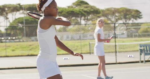 Young female tennis players practicing backhand stroke on sunny outdoor court with racket