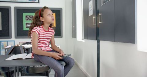 Tired girl sitting in classroom, holding tablet, taking study break