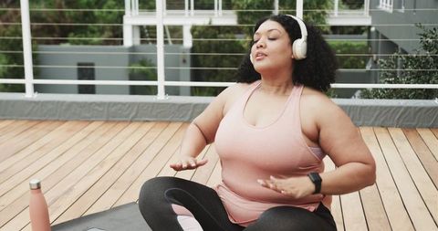 Woman Practicing Breathwork on Rooftop Terrace with Headphones, Yoga Mat and Water Bottle