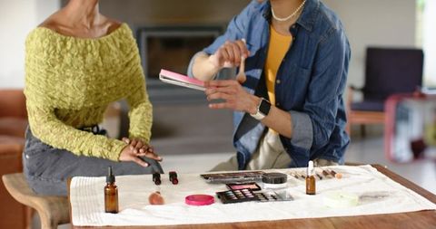 Makeup artist showing eyeshadow palette to african american client in home beauty session