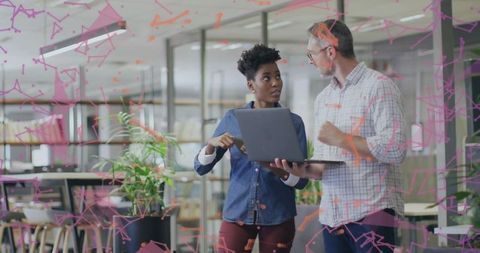 Coworkers collaborating over laptop in modern open office with glass partition graphics