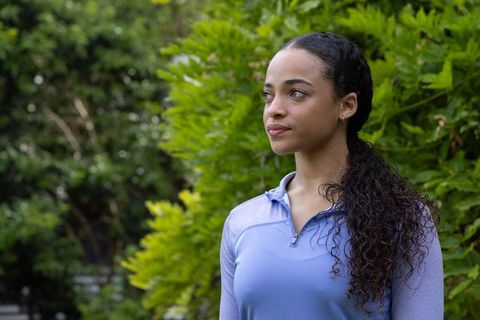 African american woman standing in garden wearing blue athletic zip top gazing thoughtfully