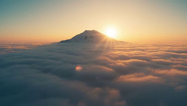 Mountaintop Illuminated by Sunrise Above Sea of Clouds