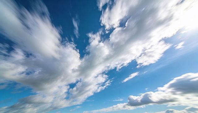 Drifting cumulus and cirrus streaking across bright blue sky with sun flare