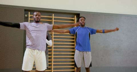 Black male athletes stretching arms in gym with wooden stall bars for team training