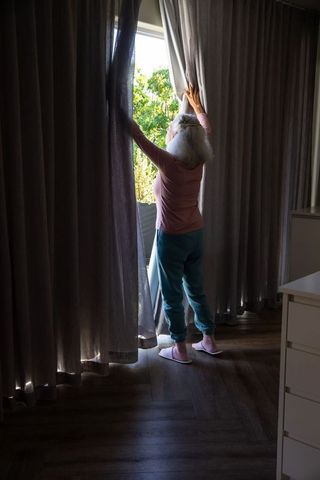 Senior opens curtains to sunlight in cozy home environment