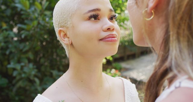 Depicts a young woman with a blonde buzz cut looking up in admiration at a friend outdoors. Nice warm, relational moment ideal for themes involving friendship, connection, and outdoor leisure activities in natural settings.