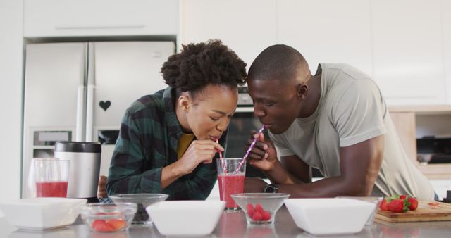Image of happy african american couple drinking homemade juice from one glass with straws. Love, relationship and spending quality time together concept.