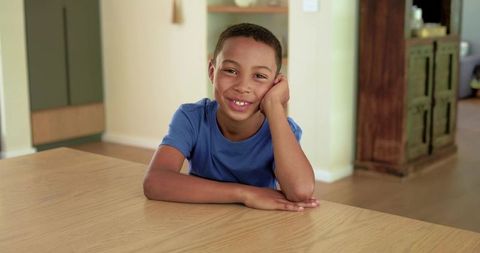 Smiling african american boy leaning on wooden table in cozy home kitchen casual portrait