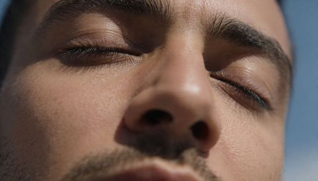 Man tilting head back with closed eyes showing skin texture, stubble, thick eyebrows