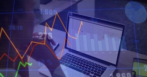 Writing business notes on laptop with financial charts and analytics overlays