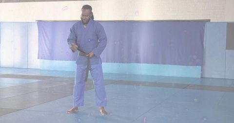 Martial artist adjusting black belt in dojo wearing blue gi and training on mats