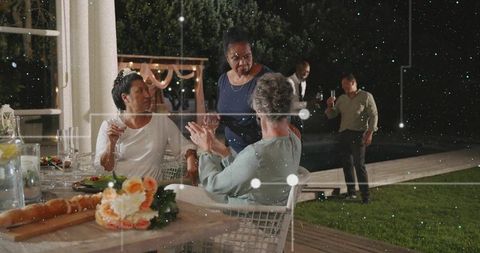 Friends chatting at elegant backyard dinner party with floral centerpiece and string lights