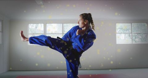 Teenage martial artist executing high side kick in blue gi with black belt in dojo