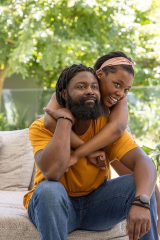 African american couple embracing on sunlit patio sofa, woman leaning playfully