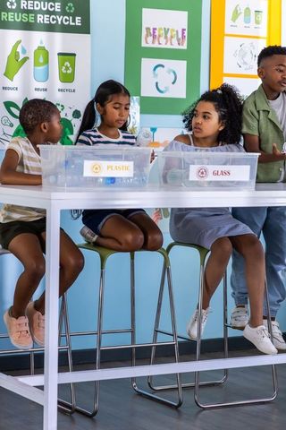 Diverse kids sorting plastic and glass recycling bins in classroom learning sustainability
