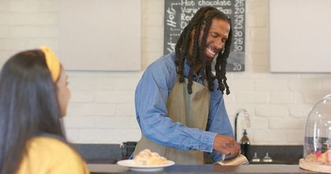 African american barista smiling while pouring milk for female customer at cozy café counter