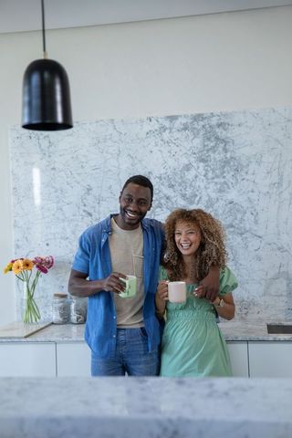 Smiling diverse couple enjoying coffee in modern marble kitchen, cozy lifestyle moment