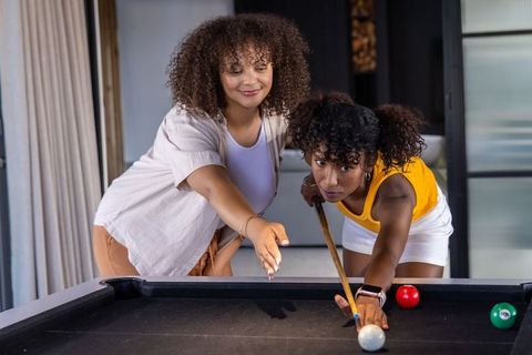 Diverse friends playing pool, guiding shot and aiming together in relaxed home lounge