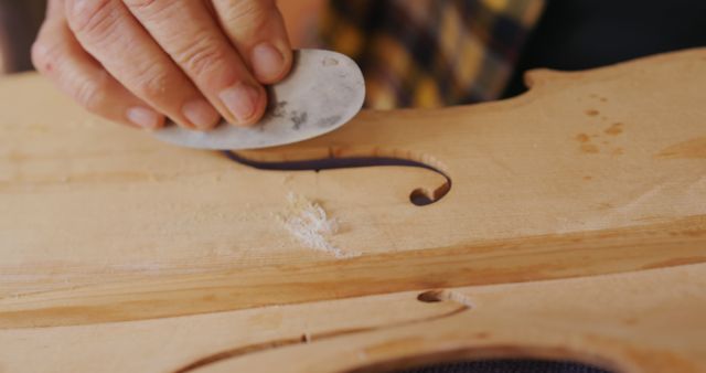 Hands of skilled woodworker carefully carving top of violin using hand tool. Ideal for showcasing traditional craftsmanship, educational content on instrument making, process of woodworking, or promoting musical artisan’s work.