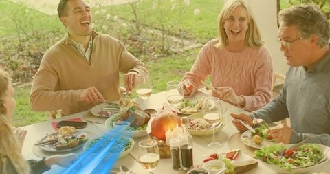 Laughing friends and family sharing sunlit autumn patio dinner with pumpkin centerpiece
