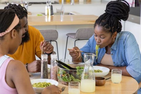 African american family enjoying pesto pasta and salad at modern kitchen table