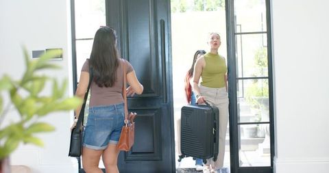 African american women entering home carrying suitcase and handbags at bright front door