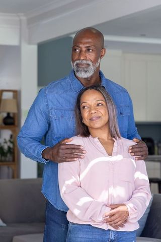 Mature couple sharing tender moment at home, man placing hands on partner's shoulders