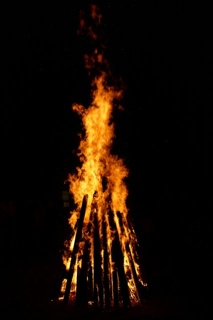 Luminous bonfire burning under the night sky, captured in vertical view. Perfect for illustrating outdoor events, campfire gatherings, or festival celebrations. Suitable for use in advertising materials, websites, or social media posts promoting outdoor activities, camping trips, or seasonal festivals.