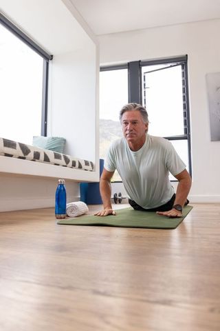 Mature man stretching on green mat in bright living room during morning home workout