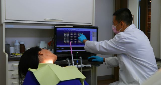 Dentist wearing a white coat and gloves explains dental x-rays to a female patient in a dental clinic. Ideal for use in health and wellness articles, dental care promotions, and educational materials about oral health and dental procedures.