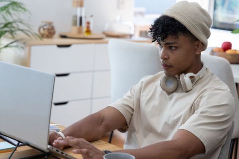 Young man working from home at dining table with laptop and headphones