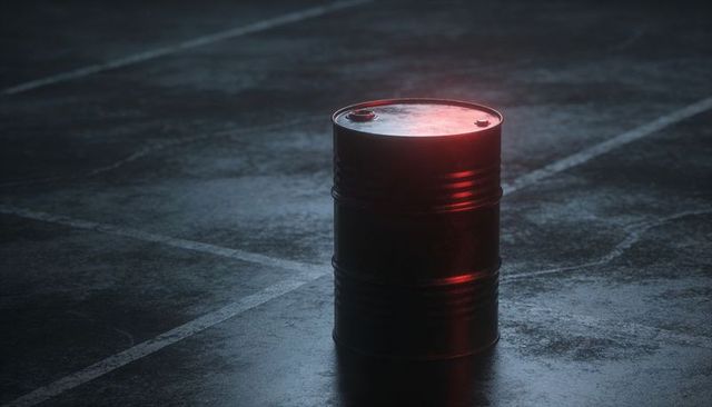 Solitary steel barrel reflecting red light on wet asphalt with painted parking lines at night