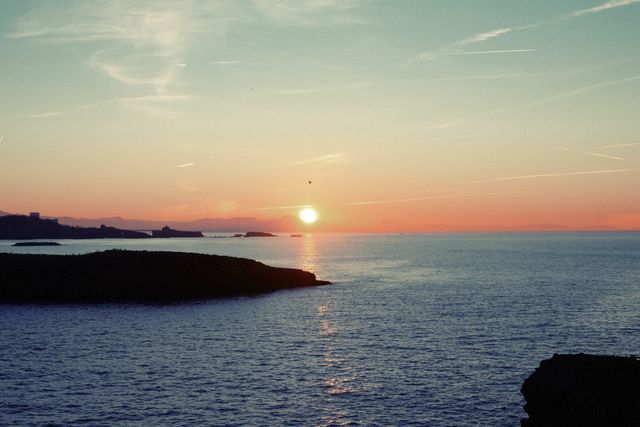 Sunset Over Calm Ocean with Silhouetted Land - Download Free Stock Photos Pikwizard.com
