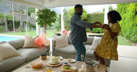 Joyful Couple Dancing at Home Celebration with Cake and Balloons