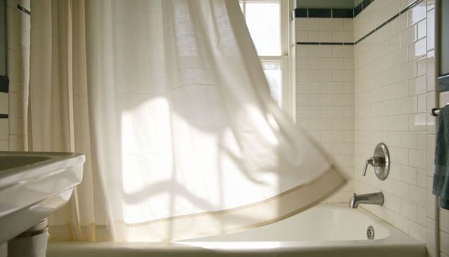 Sunlit shower curtain billowing over classic white subway-tile bathtub with chrome faucet